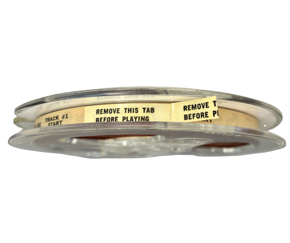 Side view of a 5-inch clear RCA Victor reel-to-reel tape with leader tab that reads “REMOVE THIS TAB BEFORE PLAYING.”